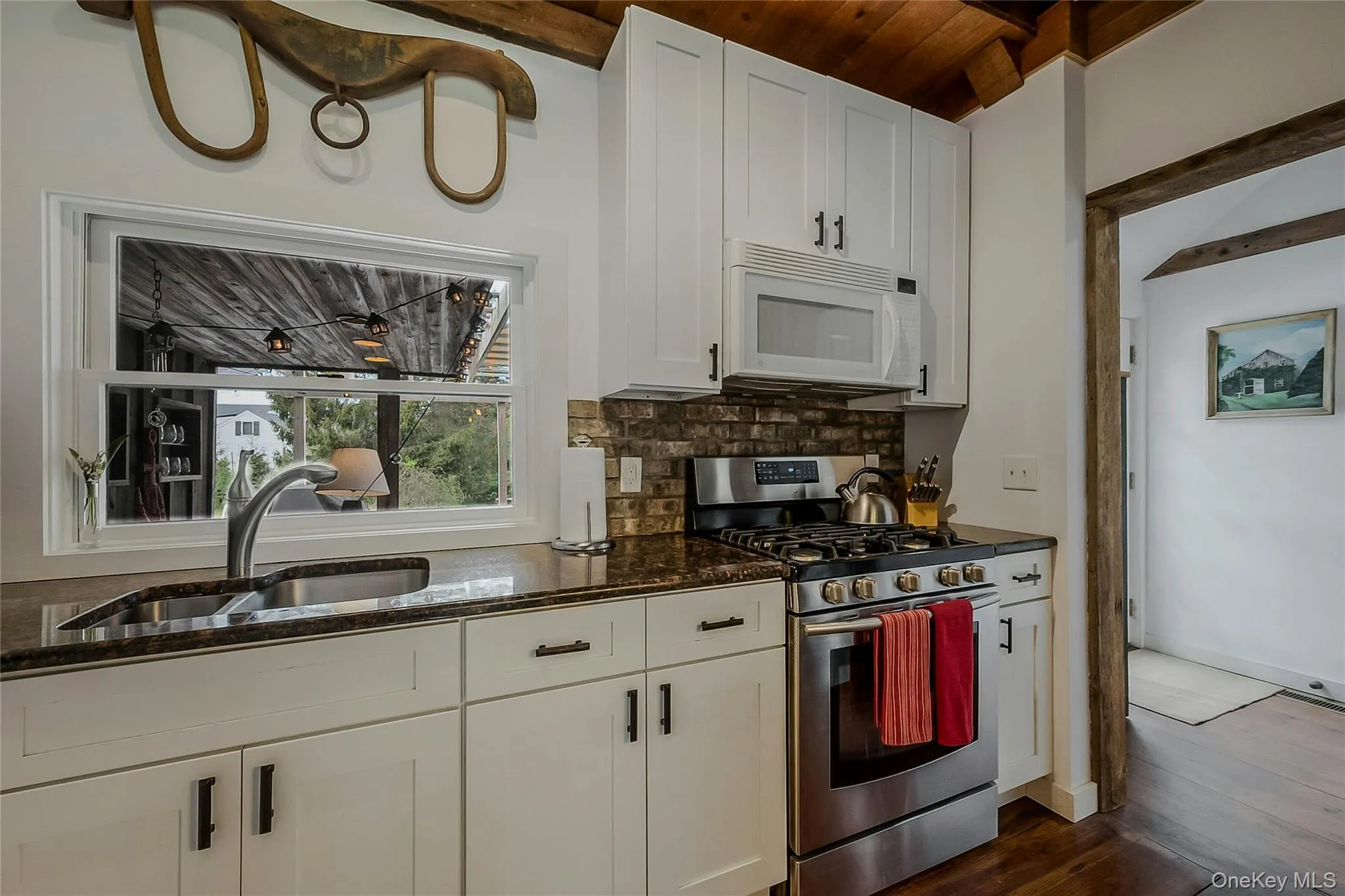 Kitchen with white microwave, gas stove, a sink, dark wood-type flooring, and dark stone countertops Kitchen with white microwave, gas stove, a sink, dark wood-type flooring, and dark stone countertops