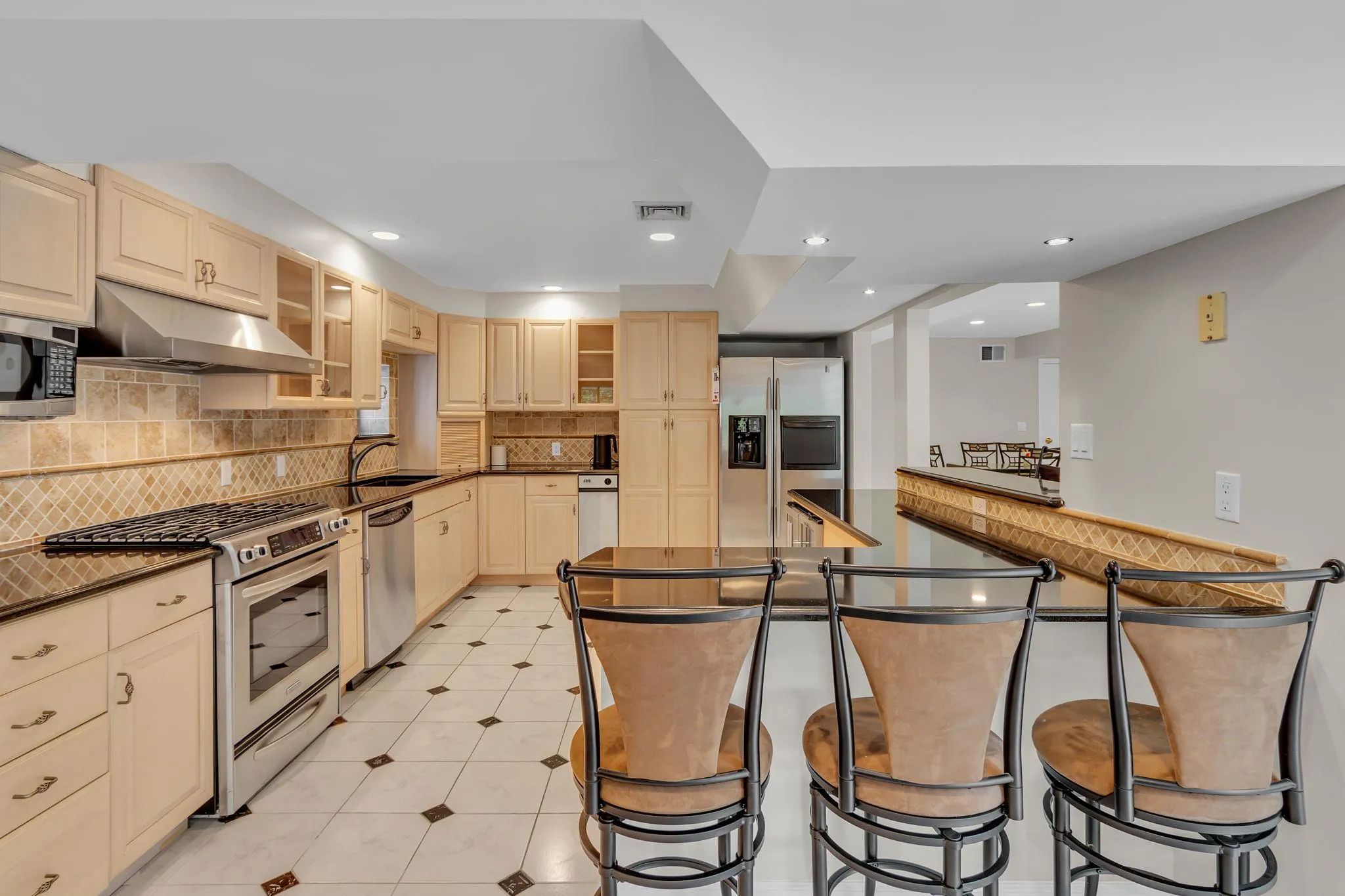 Kitchen with stainless steel appliances, under cabinet range hood, dark countertops, tasteful backsplash, and recessed lighting Kitchen with stainless steel appliances, under cabinet range hood, dark countertops, tasteful backsplash, and recessed lighting