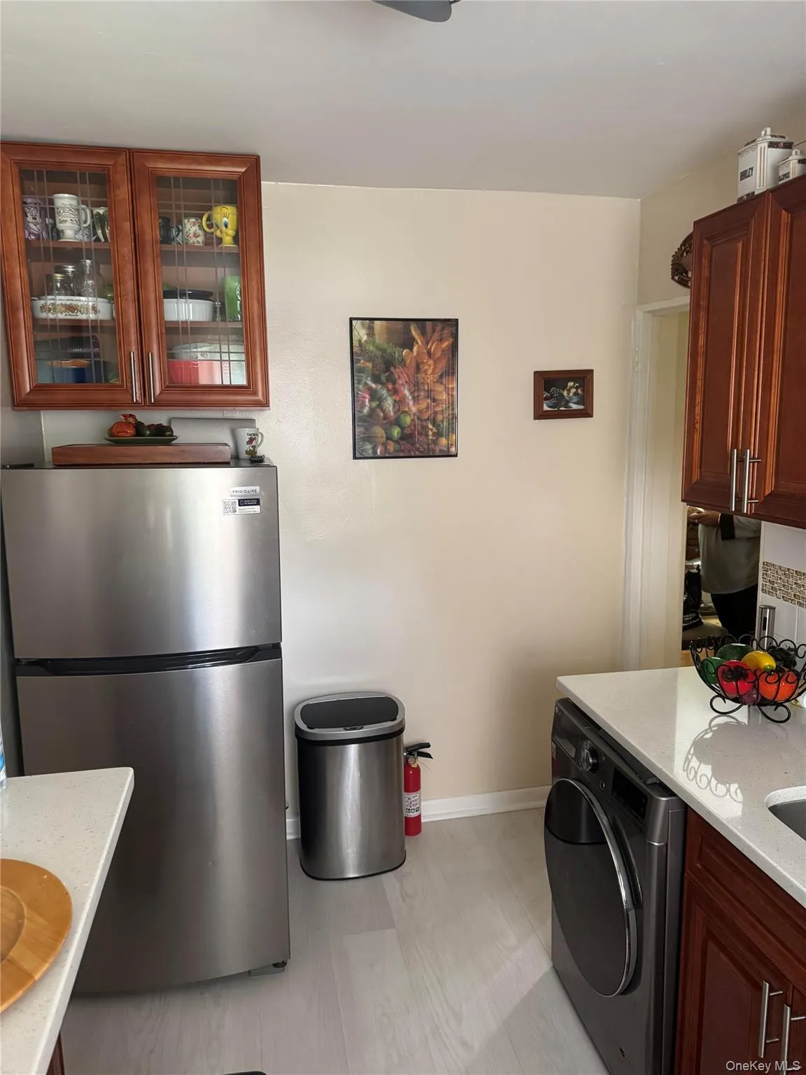 Kitchen featuring freestanding refrigerator, washer / clothes dryer, glass insert cabinets, baseboards, and light stone countertops Kitchen featuring freestanding refrigerator, washer / clothes dryer, glass insert cabinets, baseboards, and light stone countertops