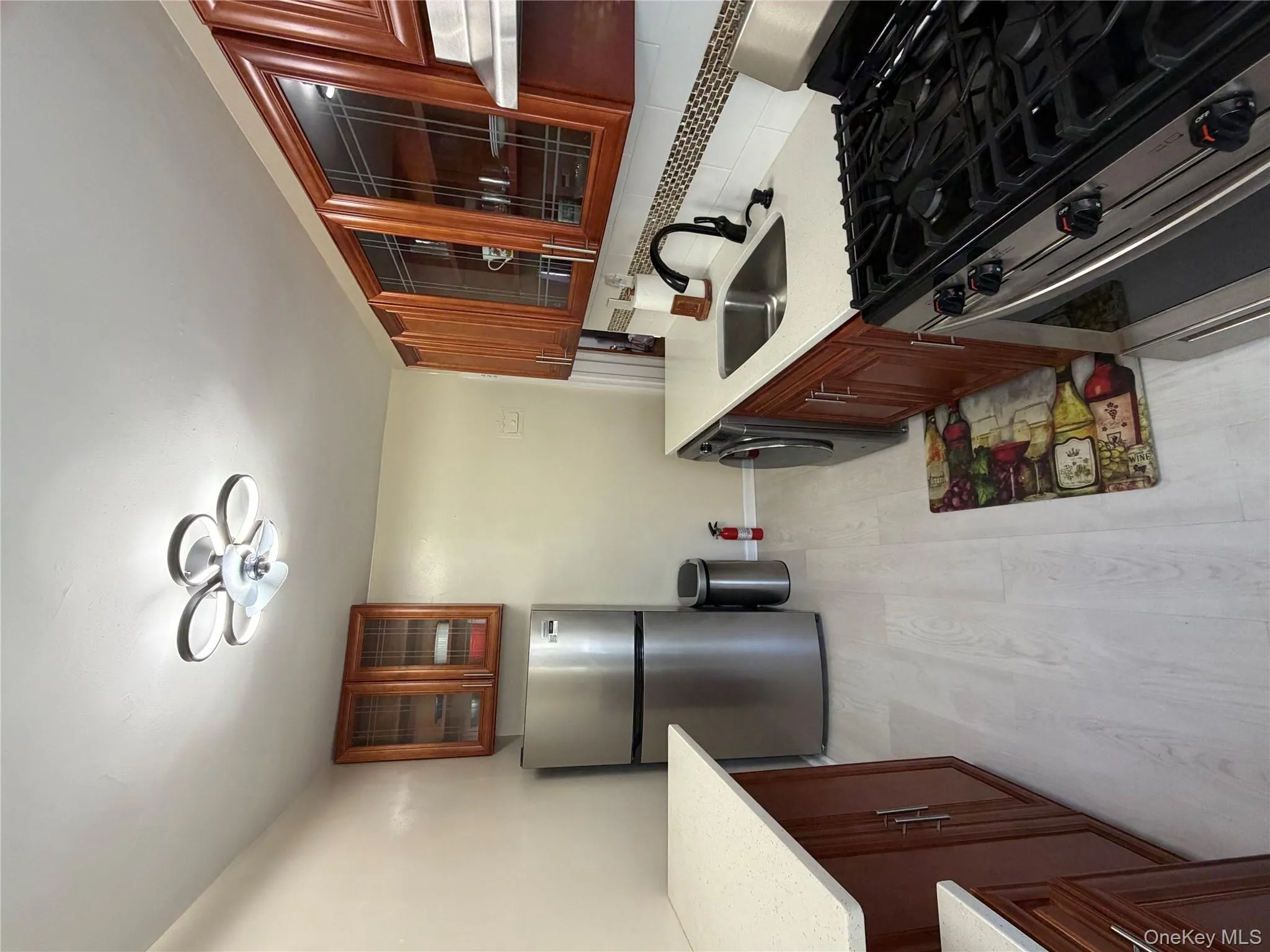 Kitchen featuring stainless steel stove, glass insert cabinets, ventilation hood, refrigerator, and light wood finished floors Kitchen featuring stainless steel stove, glass insert cabinets, ventilation hood, refrigerator, and light wood finished floors
