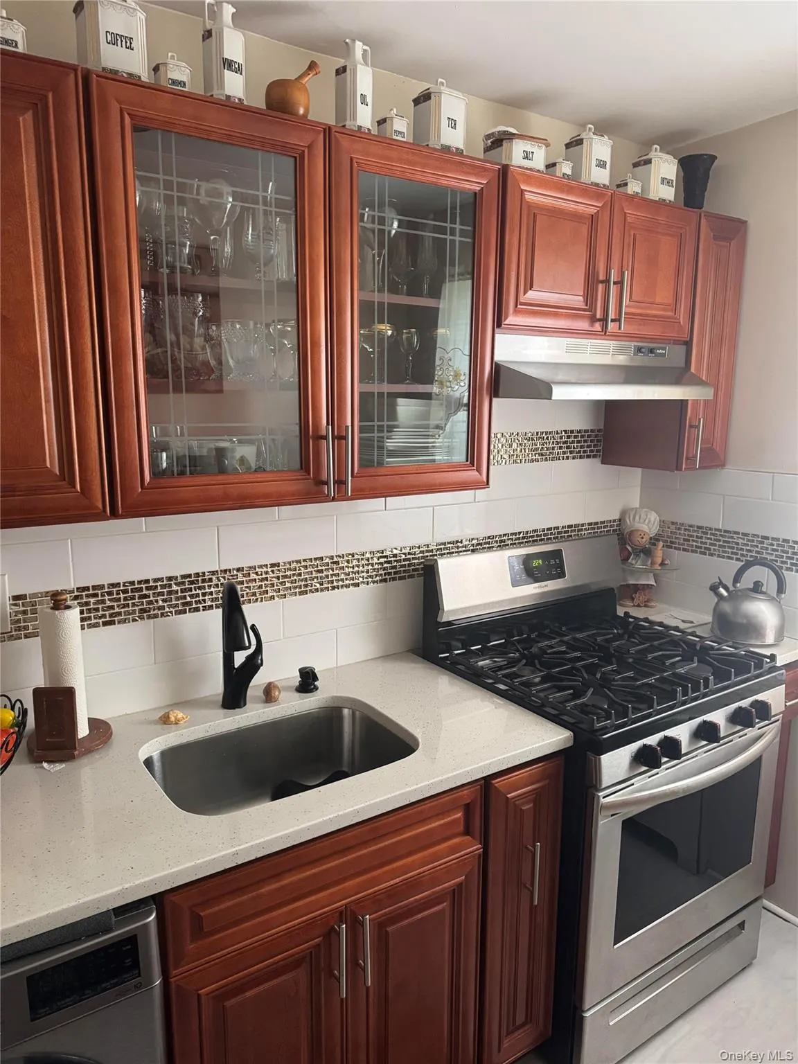 Kitchen with gas range, under cabinet range hood, a sink, backsplash, and glass insert cabinets Kitchen with gas range, under cabinet range hood, a sink, backsplash, and glass insert cabinets