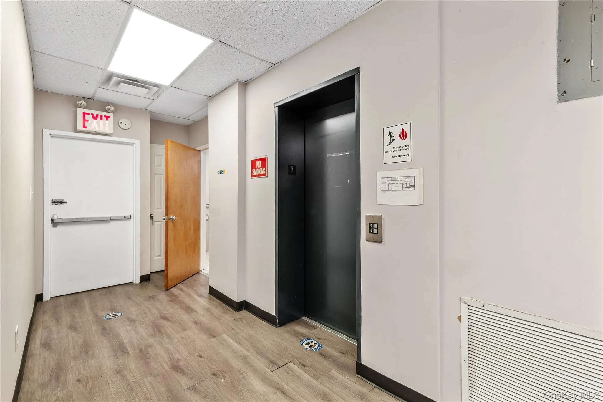 Hall featuring elevator, light wood-type flooring, electric panel, a paneled ceiling, and baseboards Hall featuring elevator, light wood-type flooring, electric panel, a paneled ceiling, and baseboards