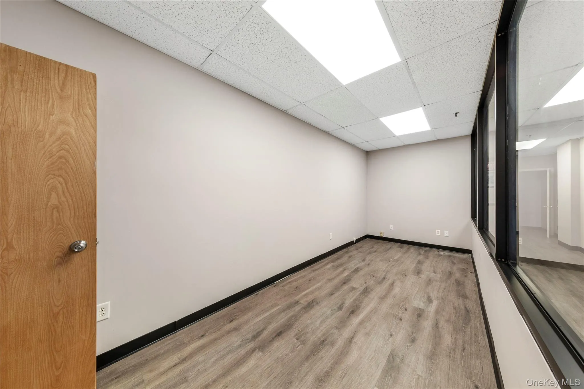 Empty room with a paneled ceiling, wood finished floors, and baseboards Empty room with a paneled ceiling, wood finished floors, and baseboards