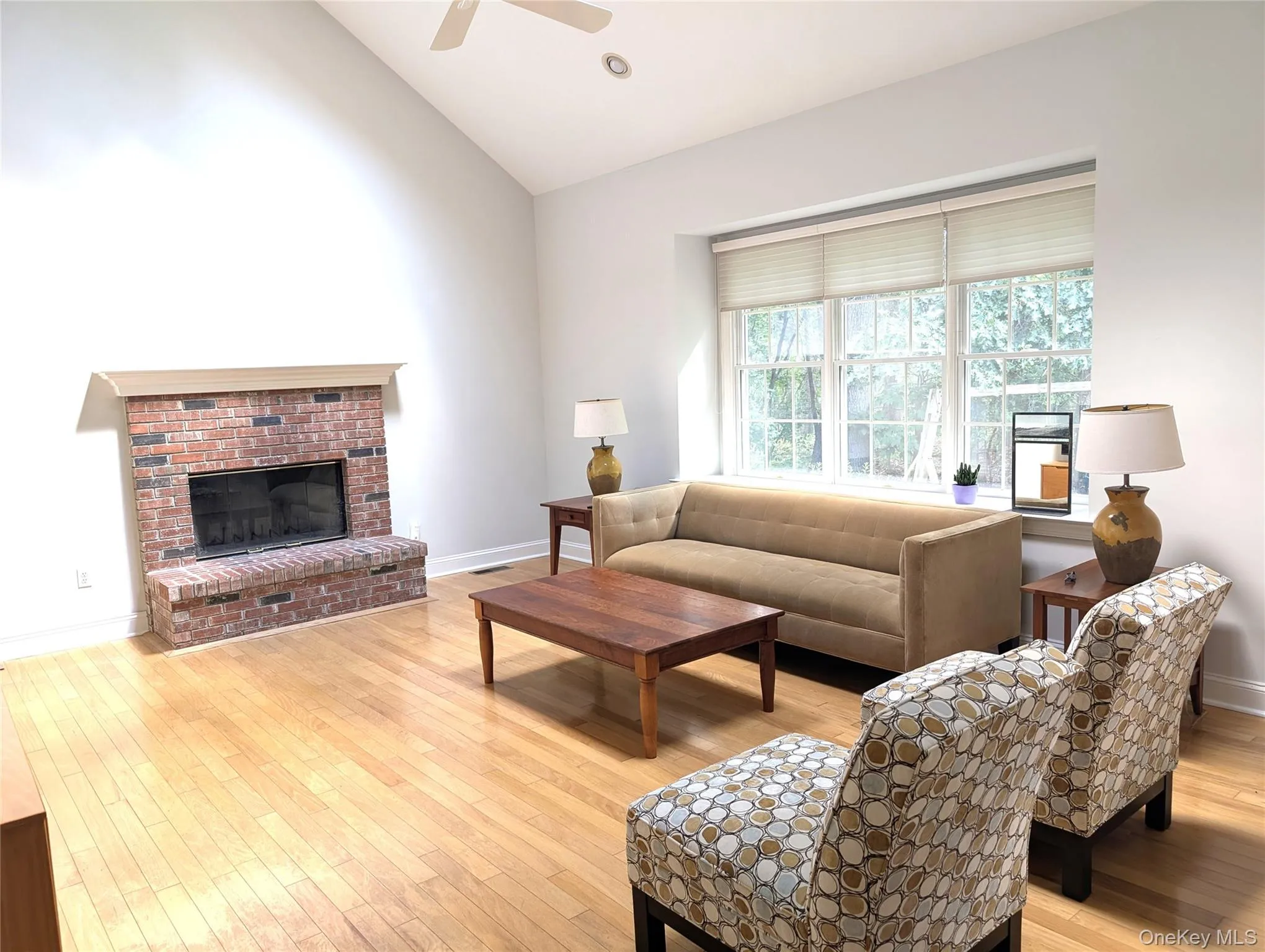 Living room with vaulted ceiling, light wood-style floors, a fireplace, and a ceiling fan Living room with vaulted ceiling, light wood-style floors, a fireplace, and a ceiling fan