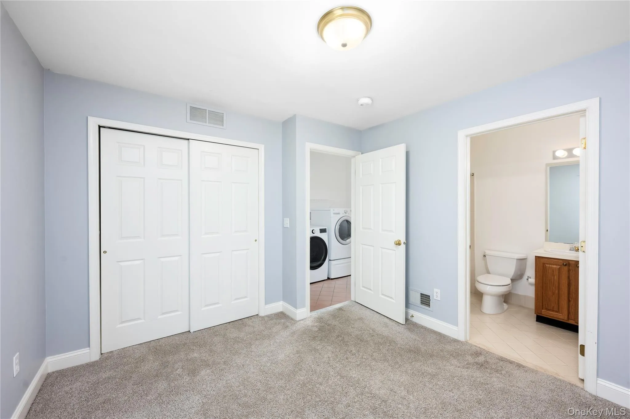 Unfurnished bedroom with washer and clothes dryer, light colored carpet, a closet, light tile patterned flooring, and ensuite bathroom Unfurnished bedroom with washer and clothes dryer, light colored carpet, a closet, light tile patterned flooring, and ensuite bathroom