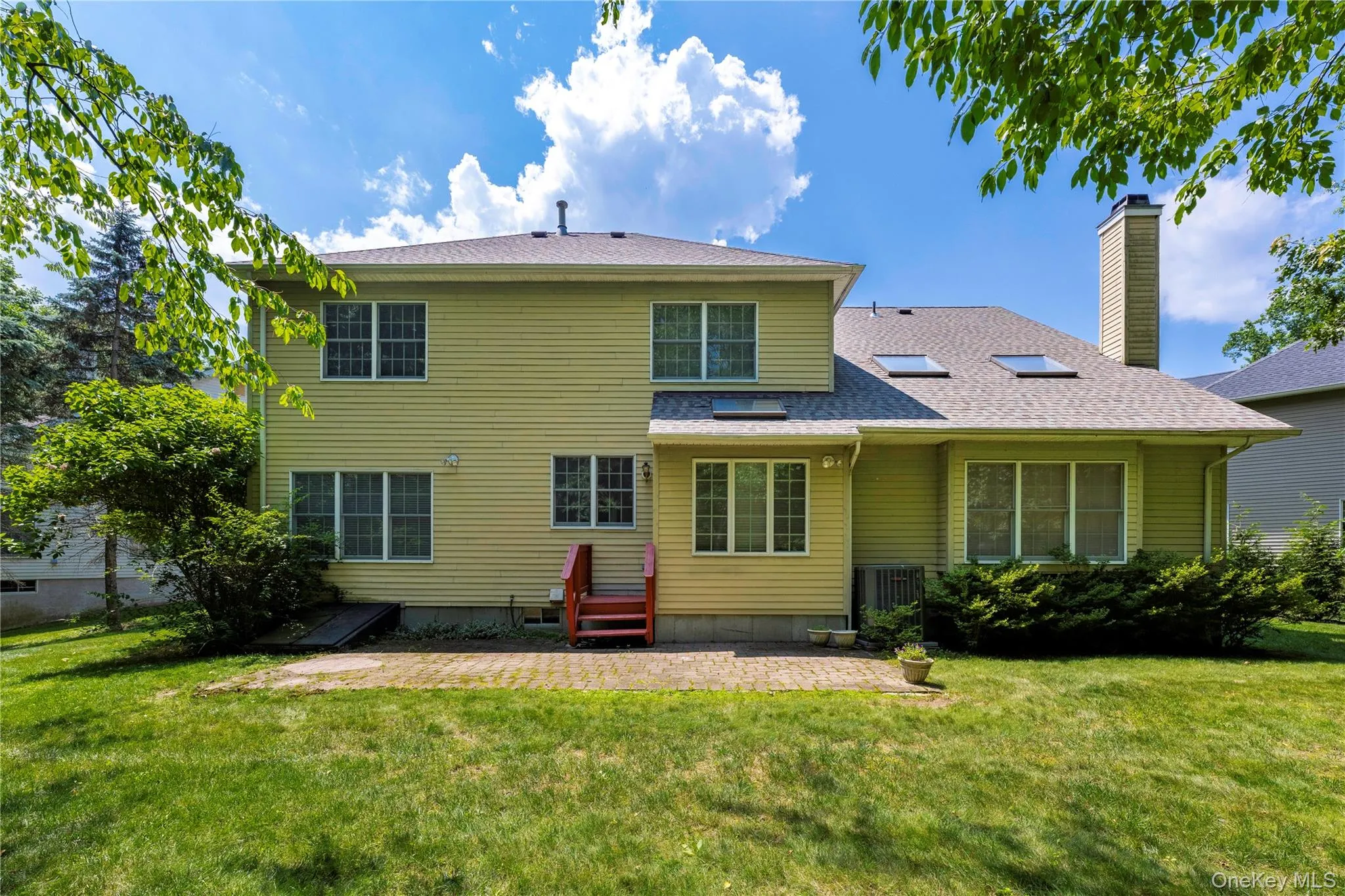 Back of house with a yard, a patio, a chimney, and roof with shingles Back of house with a yard, a patio, a chimney, and roof with shingles