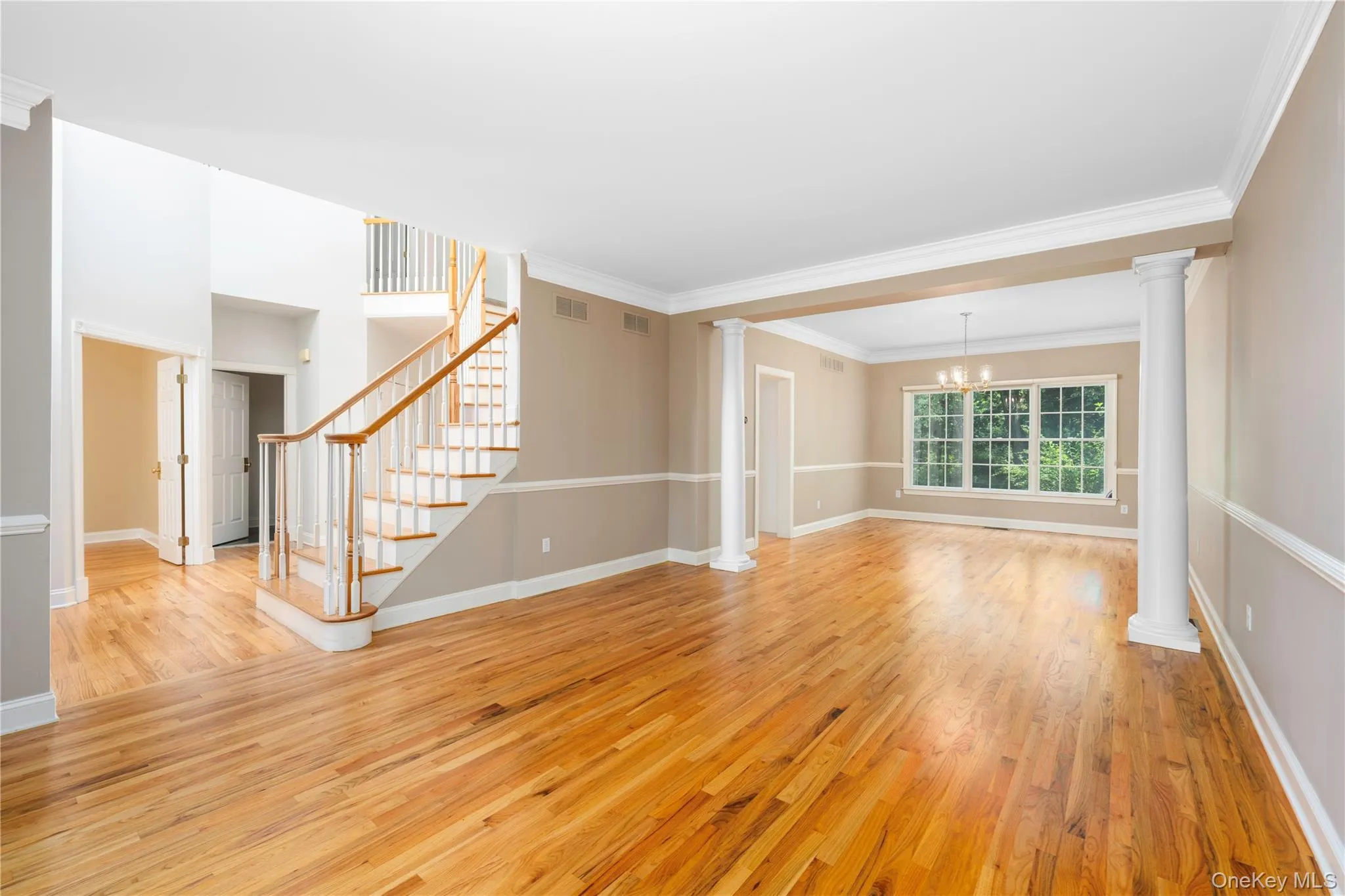 Unfurnished living room featuring light wood finished floors, a chandelier, decorative columns, and ornamental molding Unfurnished living room featuring light wood finished floors, a chandelier, decorative columns, and ornamental molding