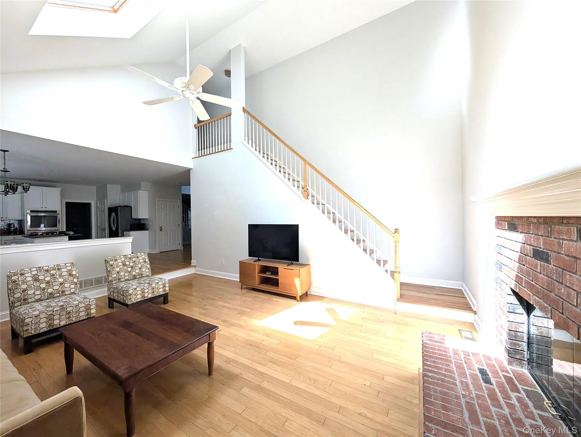 Living area featuring high vaulted ceiling, light wood-type flooring, a skylight, stairway, and a fireplace Living area featuring high vaulted ceiling, light wood-type flooring, a skylight, stairway, and a fireplace