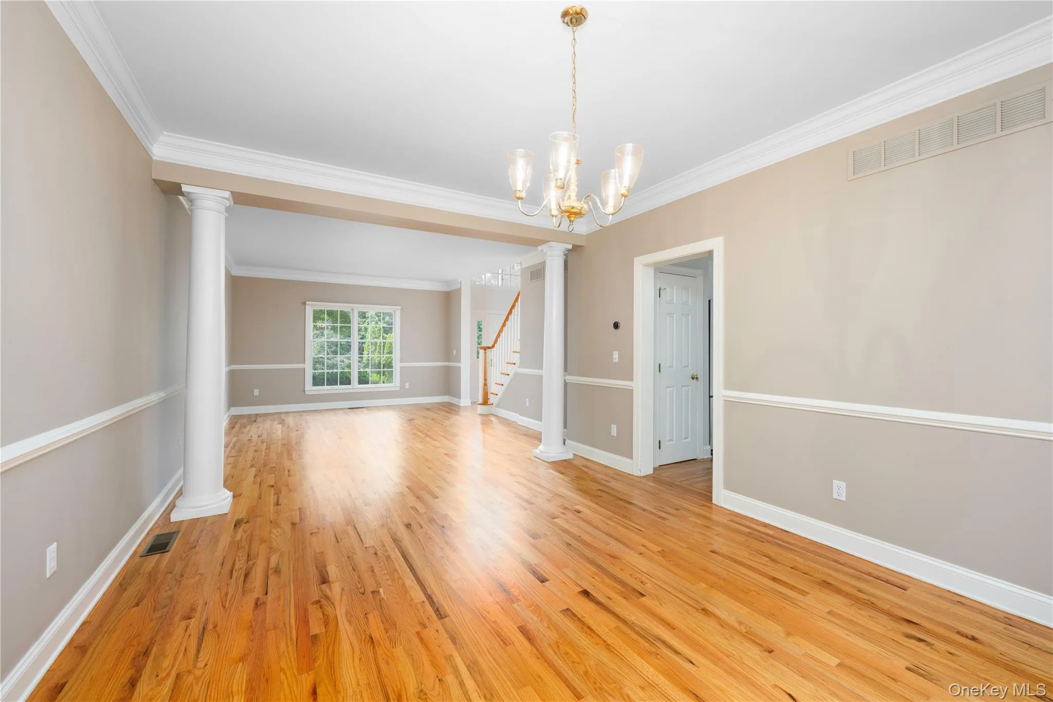 Spare room featuring light wood-type flooring, crown molding, stairs, ornate columns, and a chandelier Spare room featuring light wood-type flooring, crown molding, stairs, ornate columns, and a chandelier