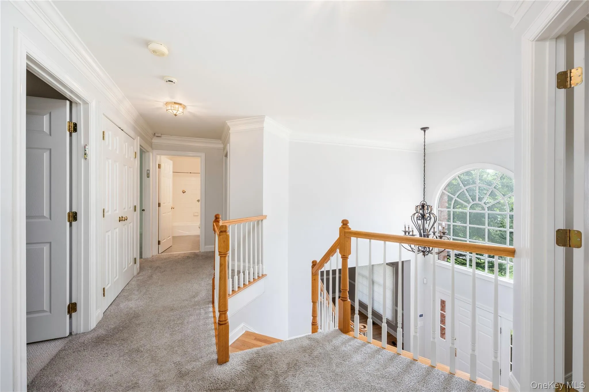 Corridor with an upstairs landing, ornamental molding, carpet flooring, and a chandelier Corridor with an upstairs landing, ornamental molding, carpet flooring, and a chandelier