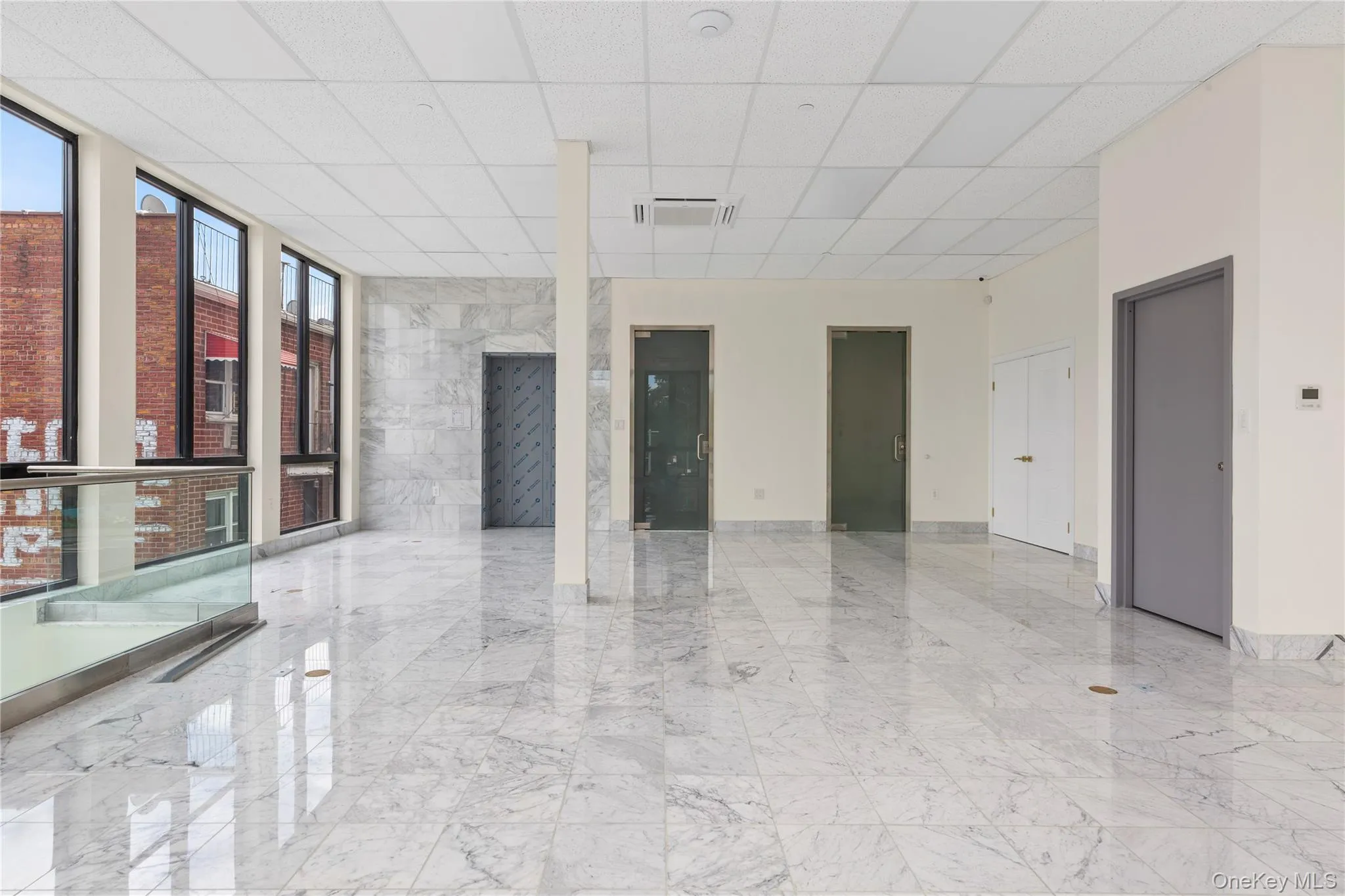 Empty room featuring marble tiled flooring, a drop ceiling, and expansive windows Empty room featuring marble tiled flooring, a drop ceiling, and expansive windows