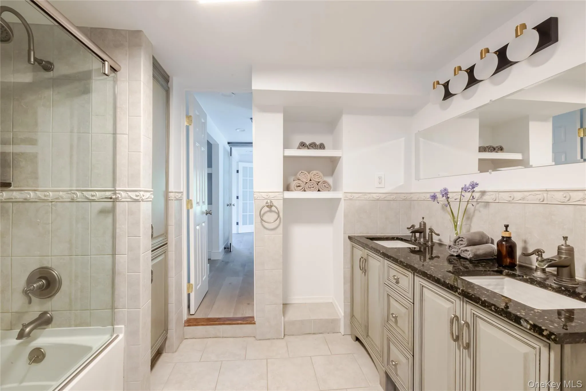 Full bath featuring tile patterned flooring, double vanity, tile walls, and enclosed tub / shower combo Full bath featuring tile patterned flooring, double vanity, tile walls, and enclosed tub / shower combo