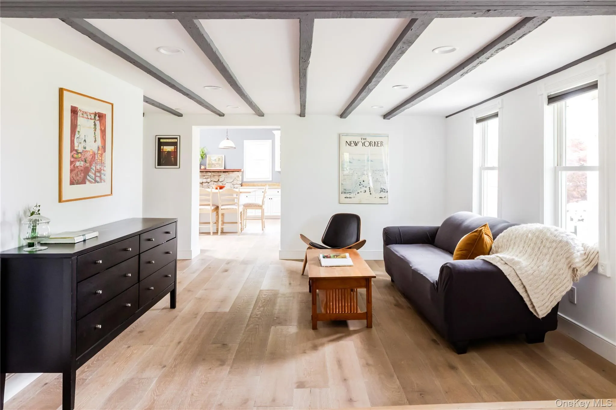 Living area featuring light wood-style floors, beam ceiling, plenty of natural light, and baseboards Living area featuring light wood-style floors, beam ceiling, plenty of natural light, and baseboards