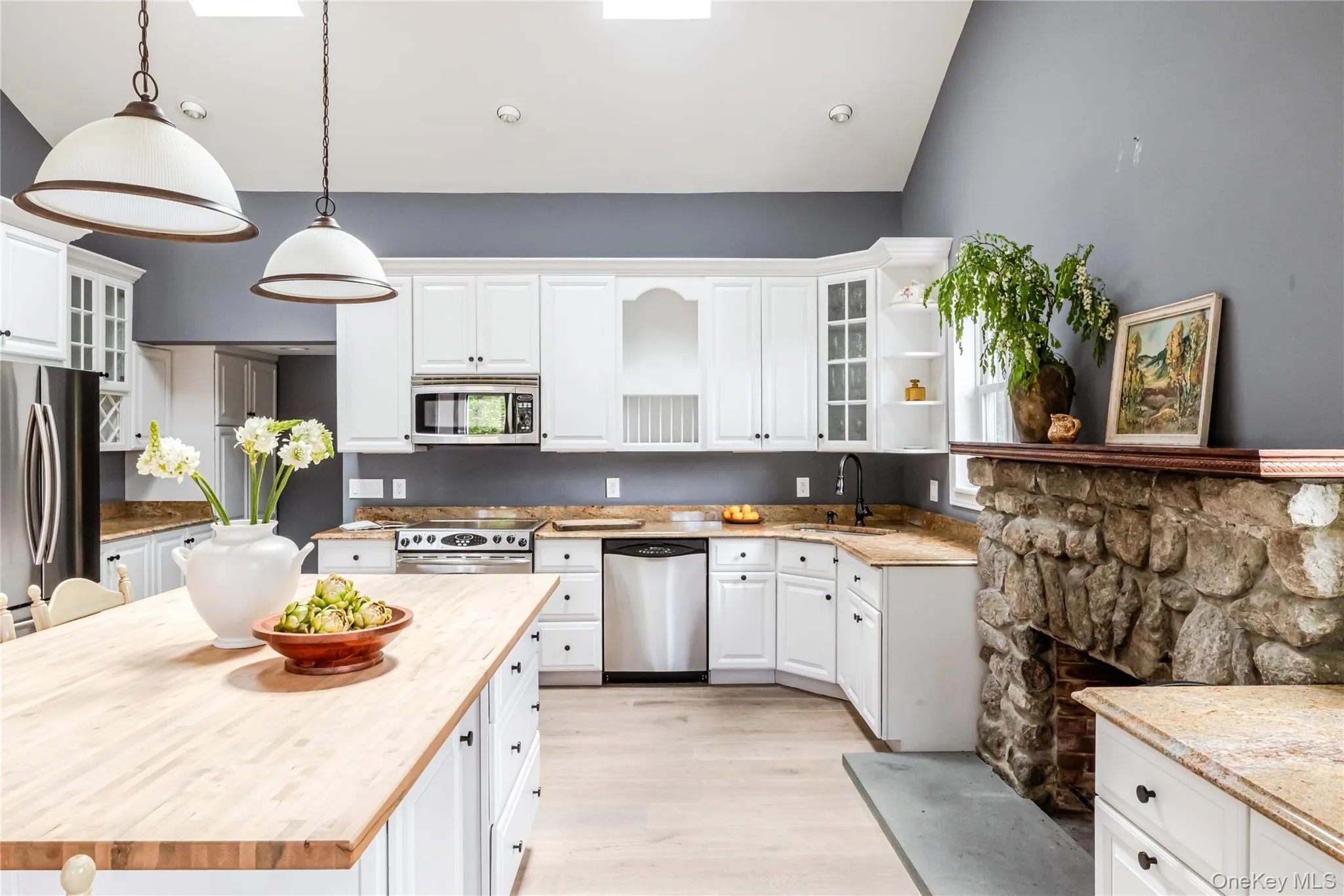 Kitchen featuring appliances with stainless steel finishes, white cabinets, a sink, light wood finished floors, and decorative light fixtures Kitchen featuring appliances with stainless steel finishes, white cabinets, a sink, light wood finished floors, and decorative light fixtures
