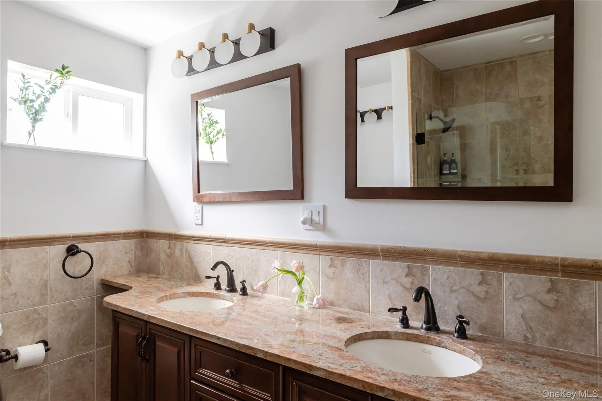 Full bath with double vanity, tiled shower, tile walls, and a wainscoted wall Full bath with double vanity, tiled shower, tile walls, and a wainscoted wall