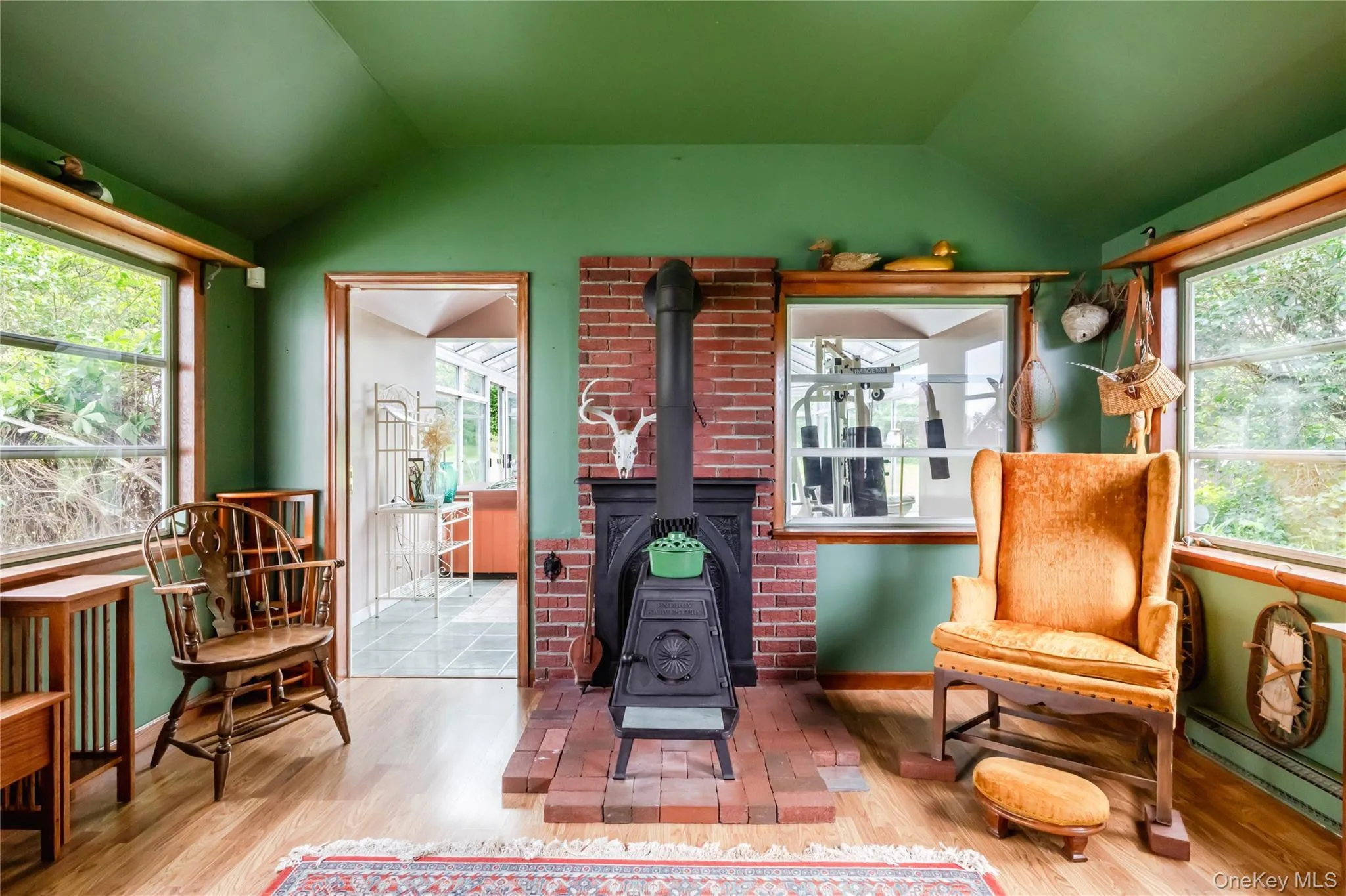 Living area featuring a wood stove, vaulted ceiling, a baseboard radiator, healthy amount of natural light, and wood finished floors Living area featuring a wood stove, vaulted ceiling, a baseboard radiator, healthy amount of natural light, and wood finished floors