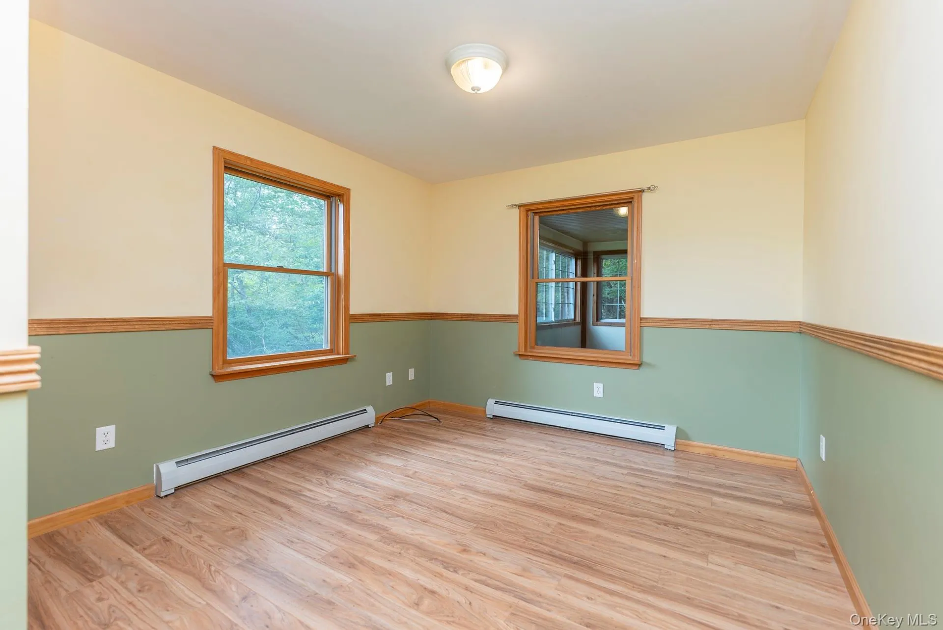 Unfurnished room with baseboard heating, wood finished floors, and baseboards Unfurnished room with baseboard heating, wood finished floors, and baseboards