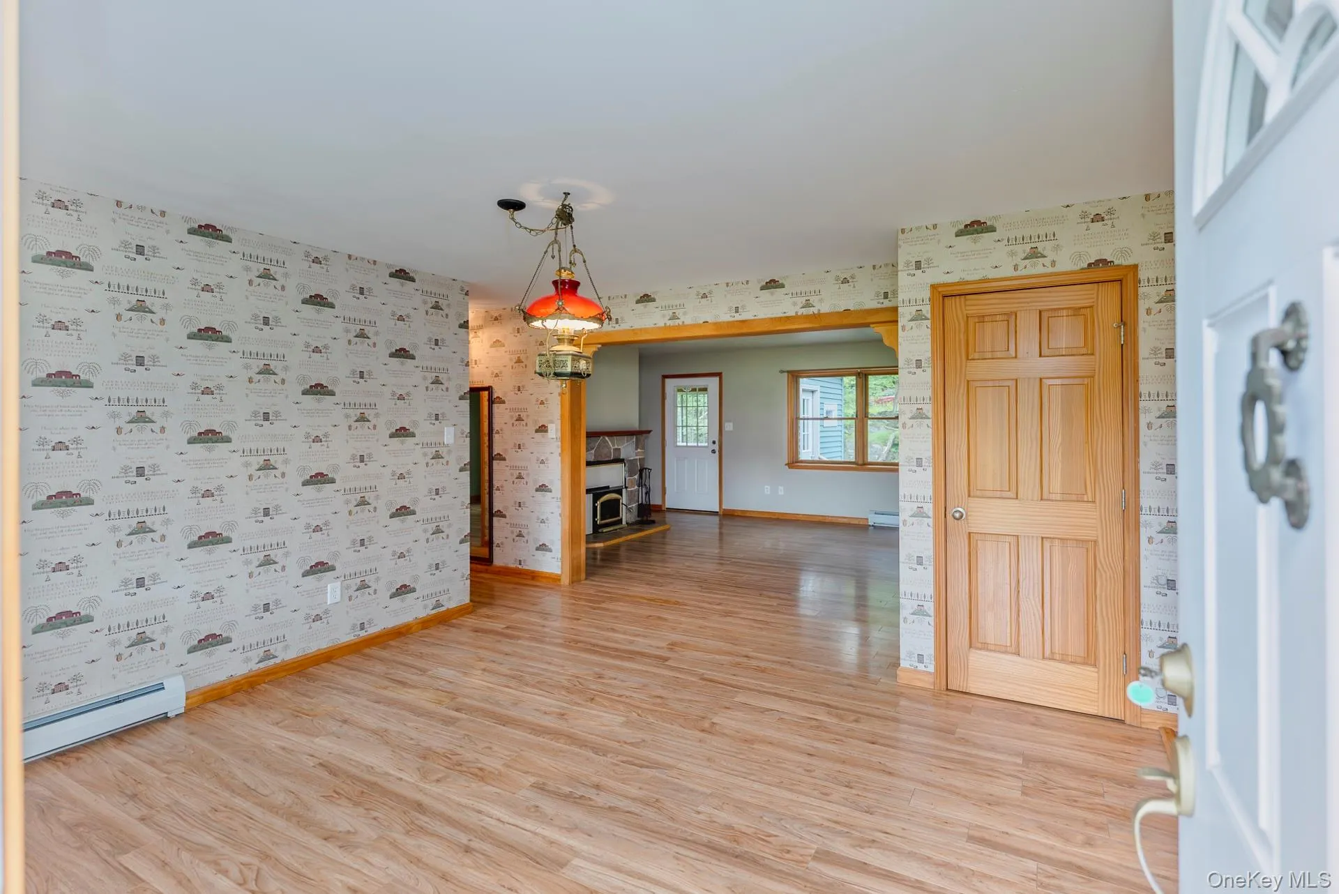 Unfurnished room featuring wallpapered walls, a baseboard heating unit, light wood-style floors, and baseboards Unfurnished room featuring wallpapered walls, a baseboard heating unit, light wood-style floors, and baseboards