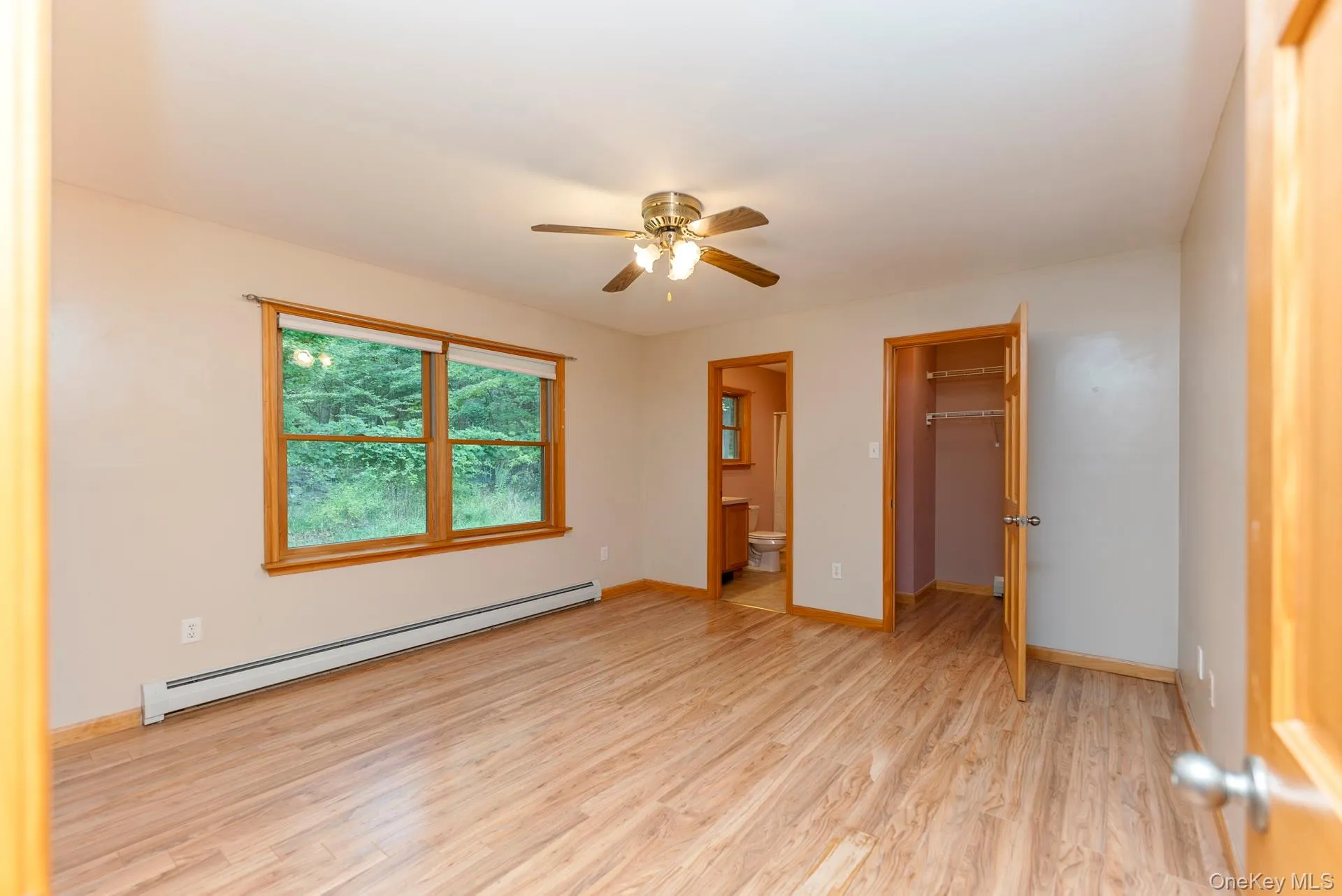 Unfurnished bedroom featuring baseboard heating, light wood-style floors, a closet, a spacious closet, and ensuite bath Unfurnished bedroom featuring baseboard heating, light wood-style floors, a closet, a spacious closet, and ensuite bath