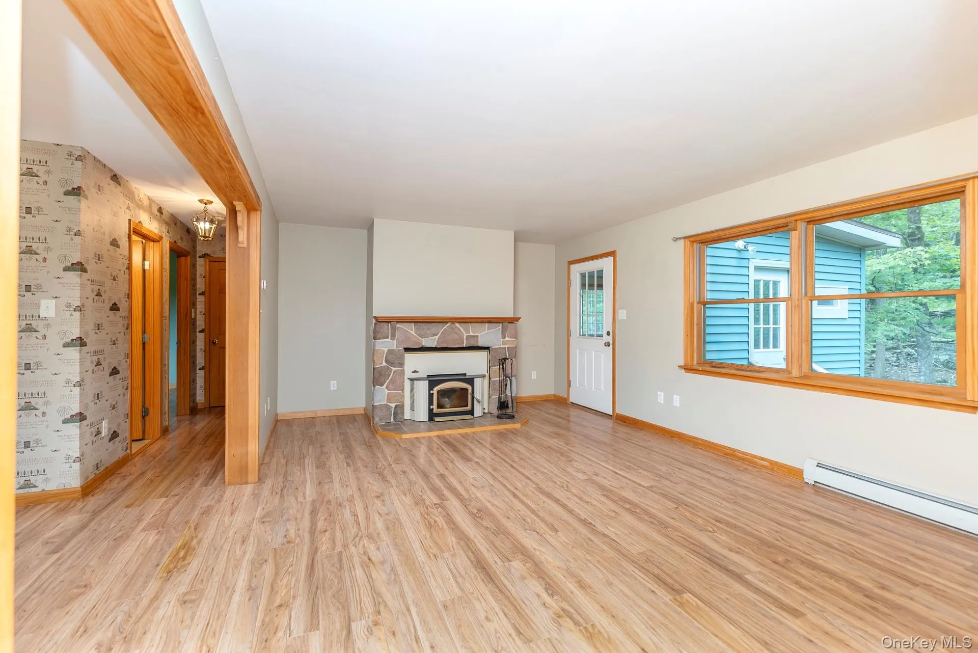 Unfurnished living room with light wood-type flooring, baseboards, and a baseboard heating unit Unfurnished living room with light wood-type flooring, baseboards, and a baseboard heating unit