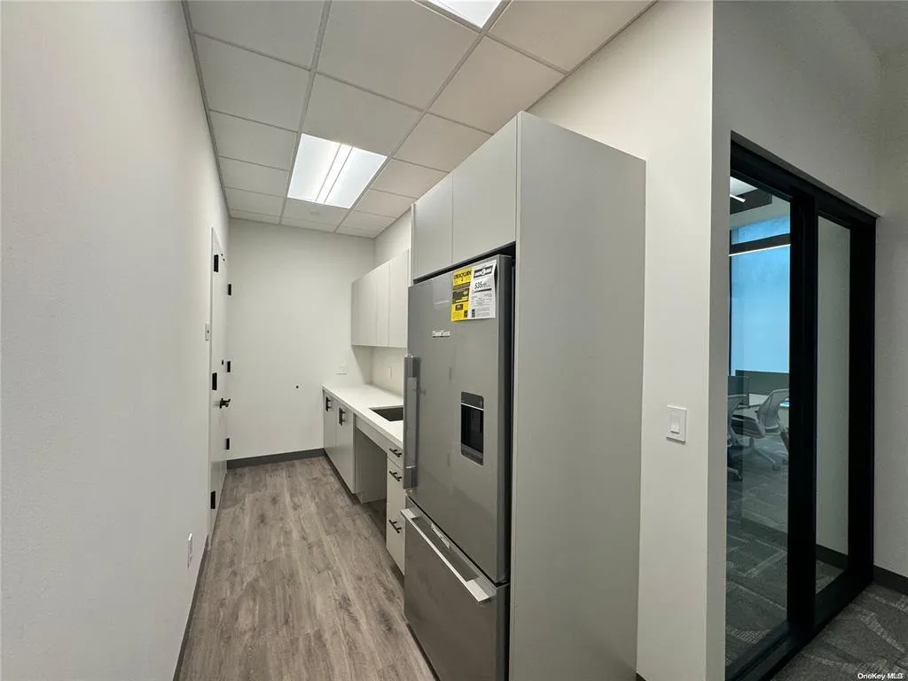 Kitchen featuring white cabinets, light wood-type flooring, light countertops, a drop ceiling, and stainless steel fridge Kitchen featuring white cabinets, light wood-type flooring, light countertops, a drop ceiling, and stainless steel fridge