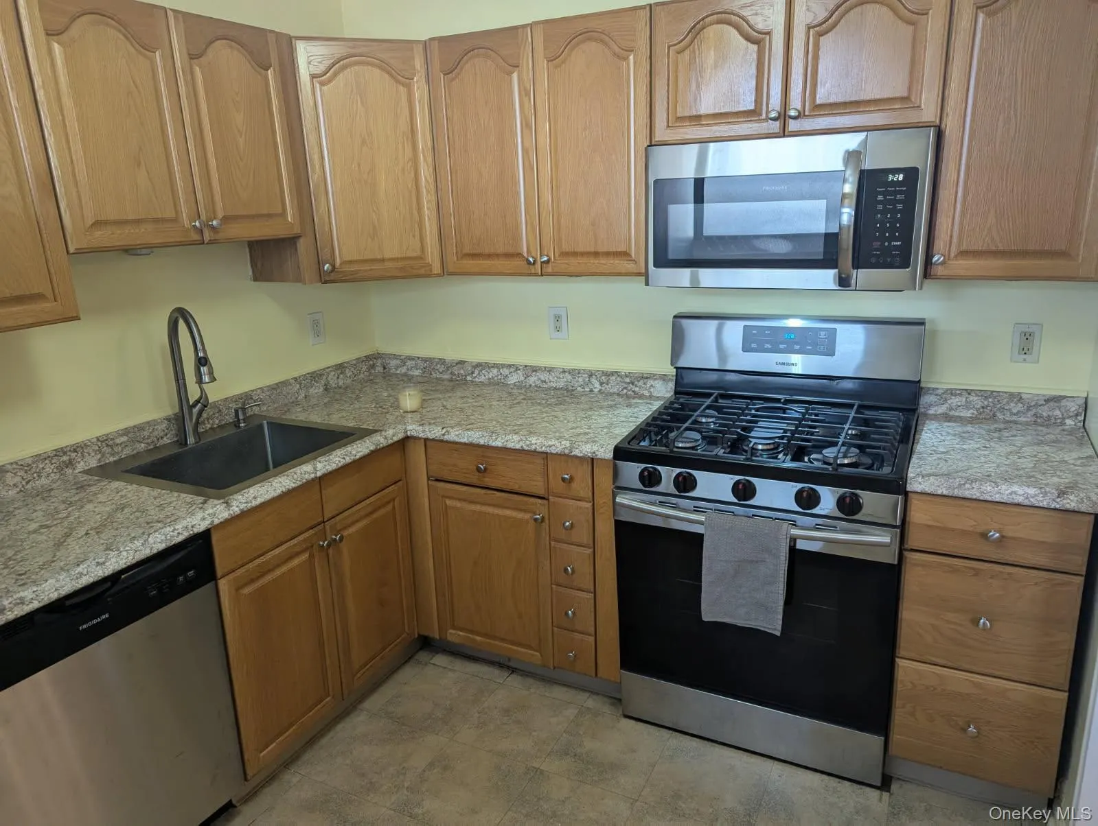 Kitchen featuring appliances with stainless steel finishes, light stone counters, and brown cabinets Kitchen featuring appliances with stainless steel finishes, light stone counters, and brown cabinets