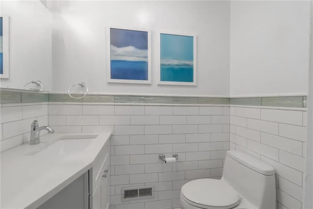 Bathroom featuring tile walls, toilet, vanity, and a wainscoted wall Bathroom featuring tile walls, toilet, vanity, and a wainscoted wall