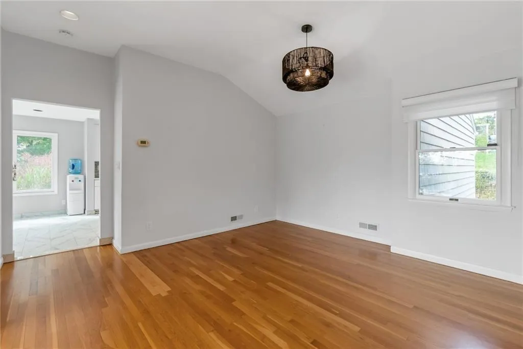 Empty room with a chandelier, light wood-style floors, lofted ceiling, baseboards, and a smoke detector Empty room with a chandelier, light wood-style floors, lofted ceiling, baseboards, and a smoke detector