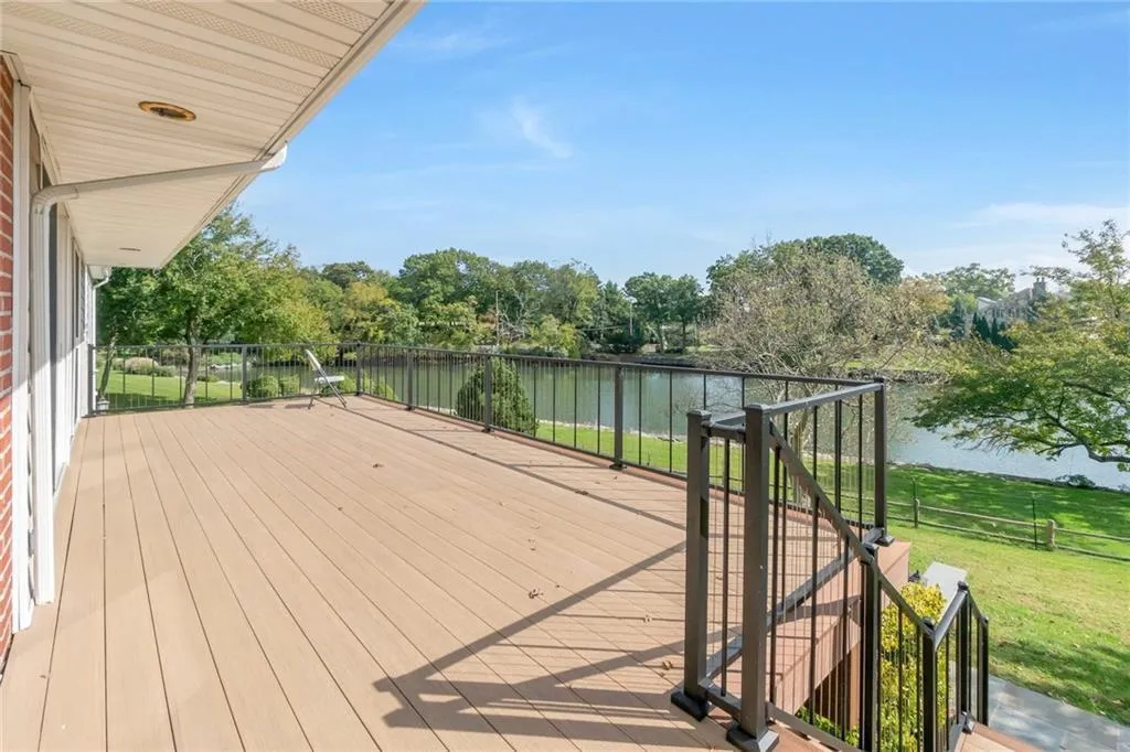 Wooden deck featuring a water view, a lawn, and view of wooded area Wooden deck featuring a water view, a lawn, and view of wooded area