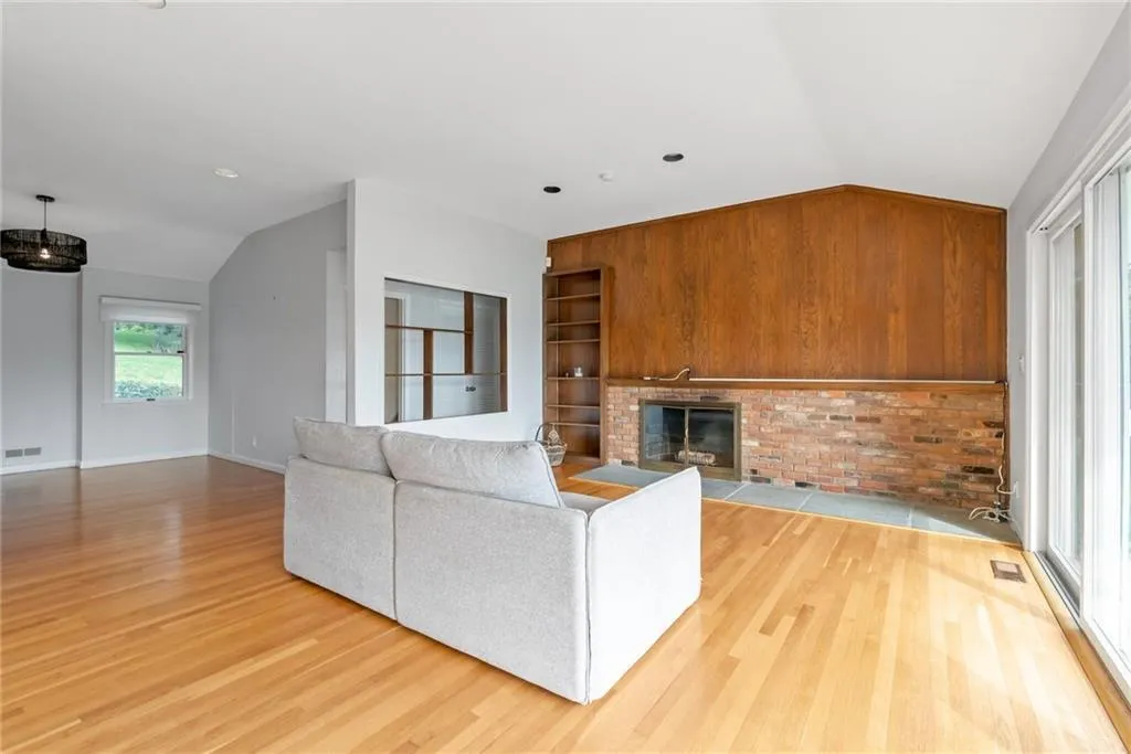 Unfurnished living room with vaulted ceiling, wood finished floors, a fireplace, and baseboards Unfurnished living room with vaulted ceiling, wood finished floors, a fireplace, and baseboards