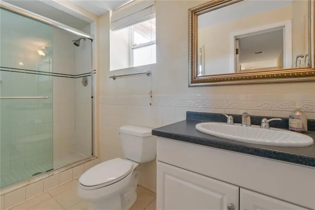 Full bathroom with toilet, vanity, a shower stall, tile patterned floors, and tile walls Full bathroom with toilet, vanity, a shower stall, tile patterned floors, and tile walls
