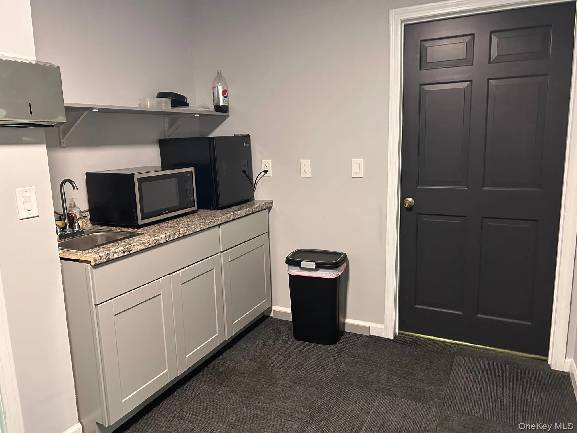 Kitchen with a sink, dark carpet, open shelves, baseboards, and light countertops Kitchen with a sink, dark carpet, open shelves, baseboards, and light countertops