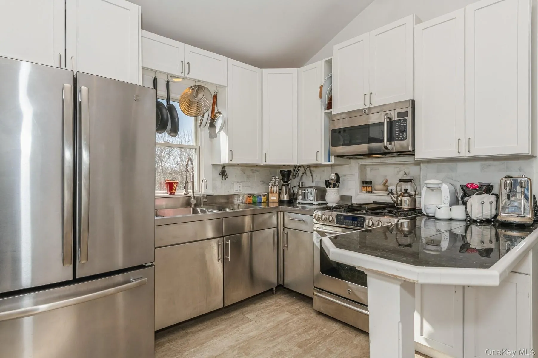 Kitchen with stainless steel appliances, white cabinetry, backsplash, lofted ceiling, and a sink Kitchen with stainless steel appliances, white cabinetry, backsplash, lofted ceiling, and a sink