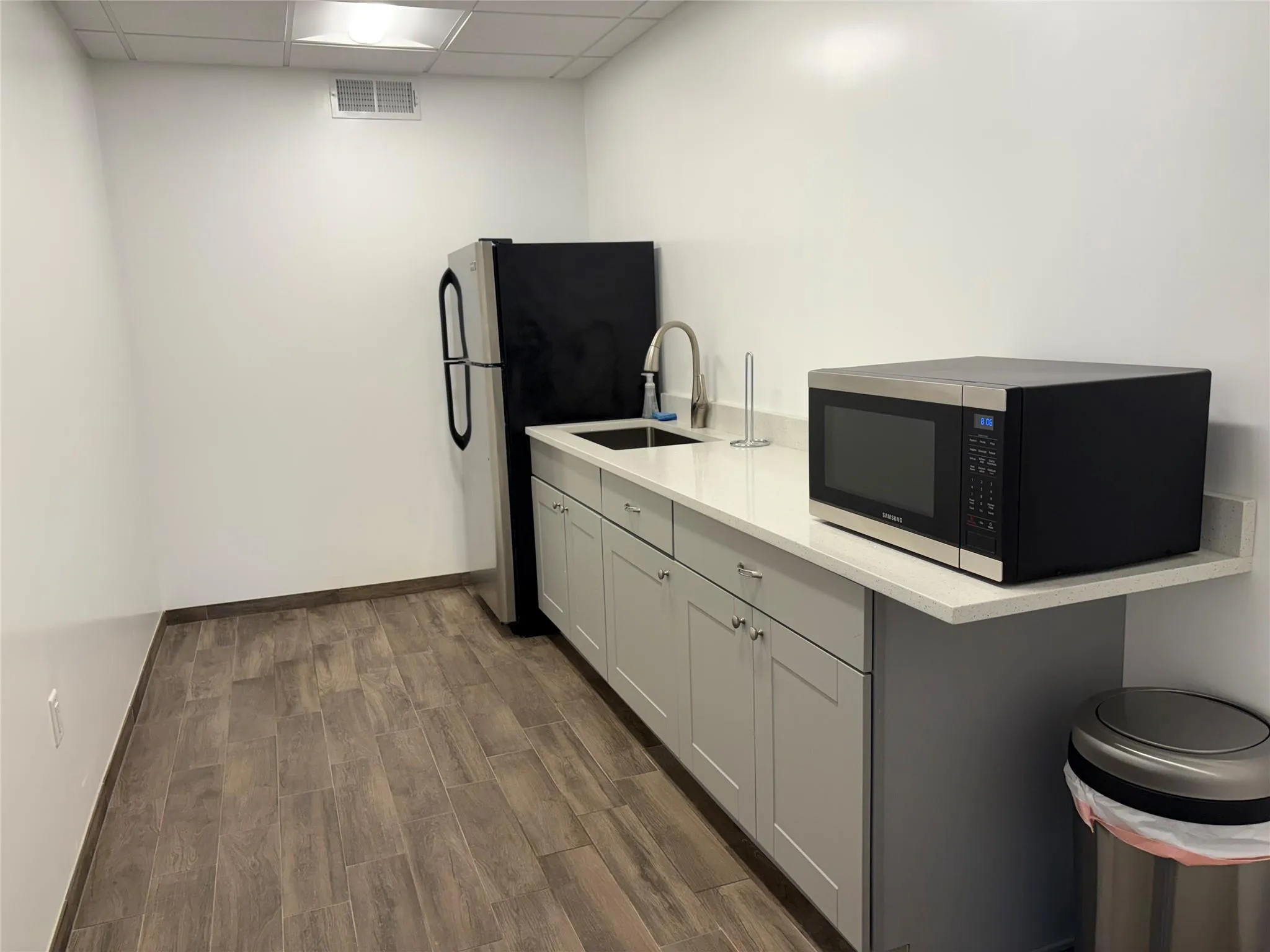 Kitchen with a sink, a drop ceiling, light countertops, freestanding refrigerator, and dark wood-style flooring Kitchen with a sink, a drop ceiling, light countertops, freestanding refrigerator, and dark wood-style flooring