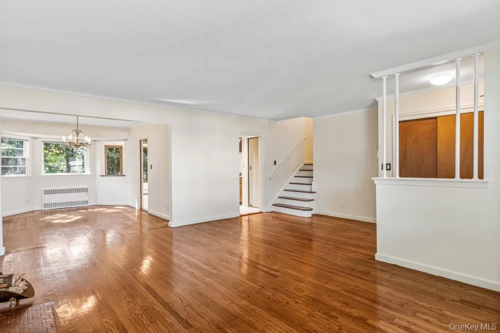 Unfurnished living room featuring wood finished floors, radiator, stairway, and a chandelier Unfurnished living room featuring wood finished floors, radiator, stairway, and a chandelier