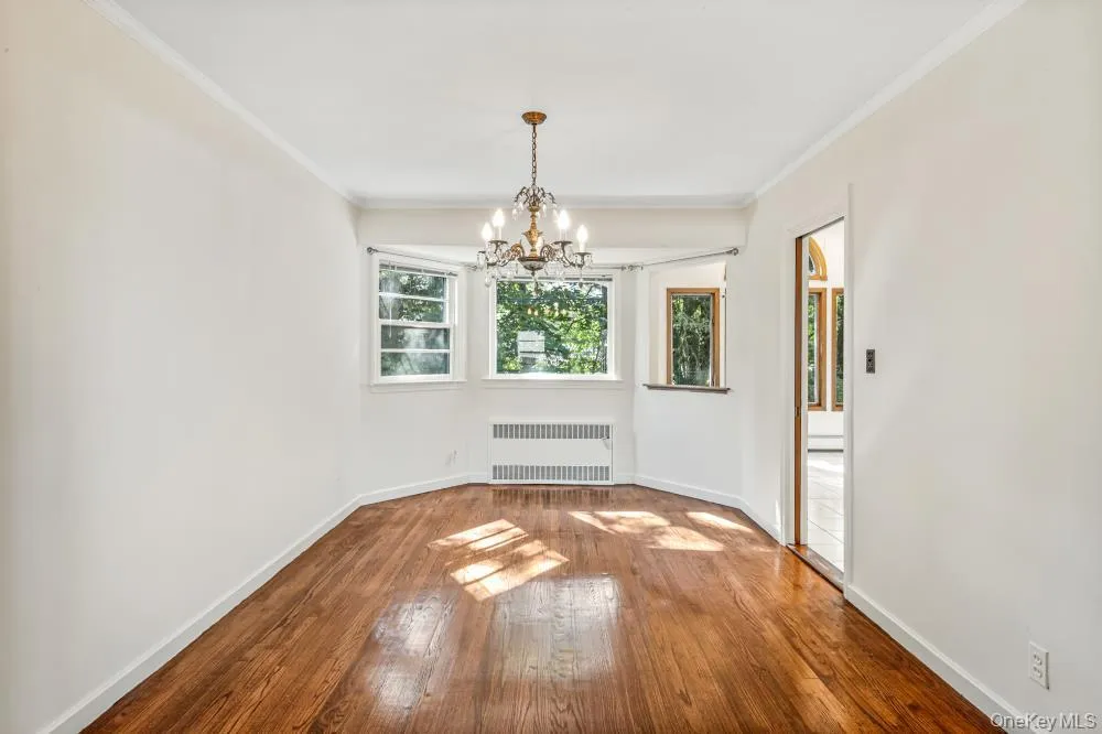 Unfurnished dining area with crown molding, hardwood / wood-style flooring, radiator heating unit, and a chandelier Unfurnished dining area with crown molding, hardwood / wood-style flooring, radiator heating unit, and a chandelier