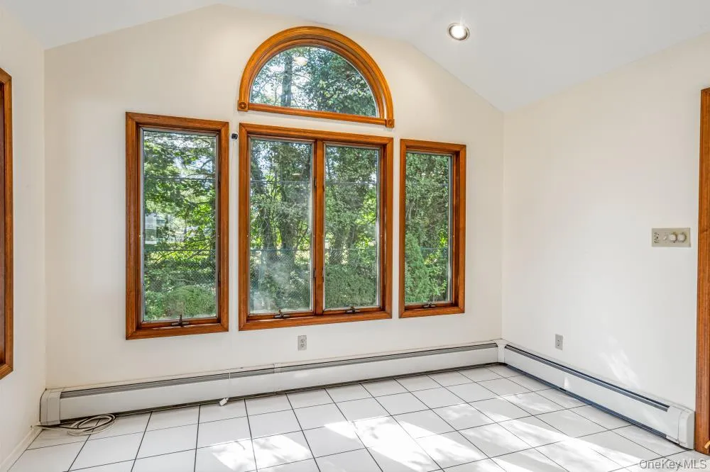 Empty room with baseboard heating, lofted ceiling, light tile patterned floors, and recessed lighting Empty room with baseboard heating, lofted ceiling, light tile patterned floors, and recessed lighting