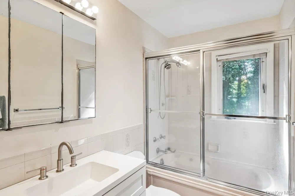 Bathroom featuring combined bath / shower with glass door, vanity, tile walls, backsplash, and a wainscoted wall Bathroom featuring combined bath / shower with glass door, vanity, tile walls, backsplash, and a wainscoted wall