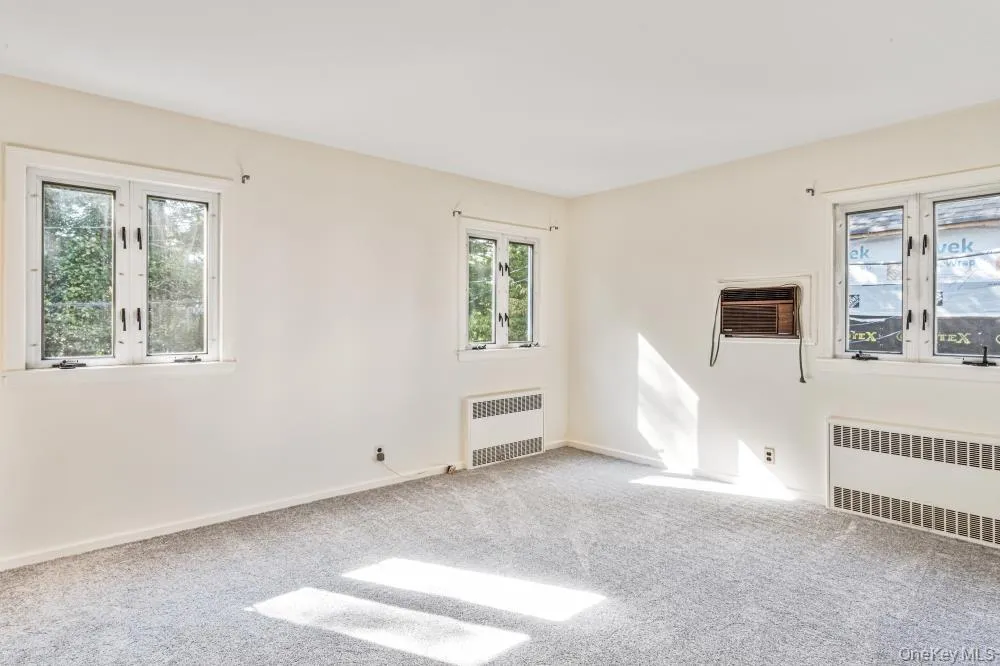 Spare room featuring carpet flooring, radiator, and a wall unit AC Spare room featuring carpet flooring, radiator, and a wall unit AC
