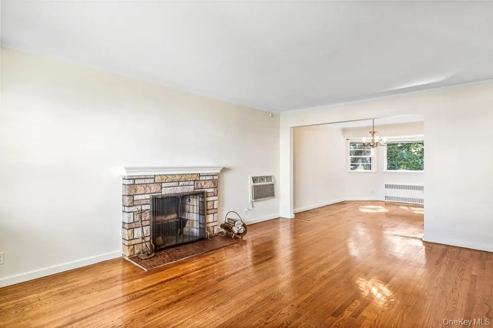 Unfurnished living room with a stone fireplace, wood finished floors, radiator heating unit, and a chandelier Unfurnished living room with a stone fireplace, wood finished floors, radiator heating unit, and a chandelier