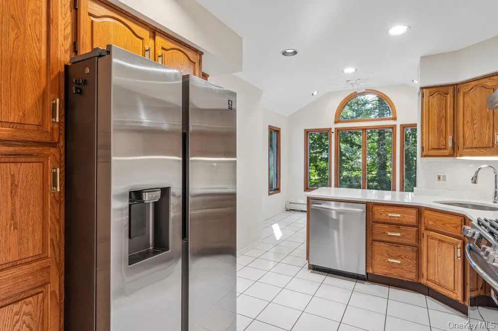 Kitchen featuring brown cabinetry, appliances with stainless steel finishes, light tile patterned floors, lofted ceiling, and a peninsula Kitchen featuring brown cabinetry, appliances with stainless steel finishes, light tile patterned floors, lofted ceiling, and a peninsula
