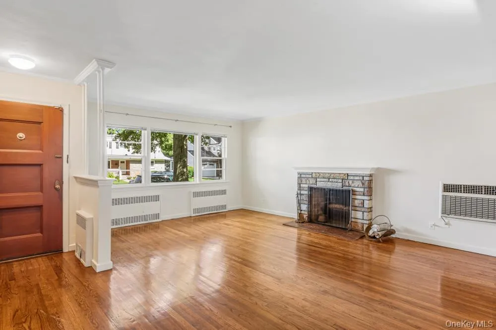 Unfurnished living room with wood finished floors, a fireplace, radiator heating unit, and ornamental molding Unfurnished living room with wood finished floors, a fireplace, radiator heating unit, and ornamental molding