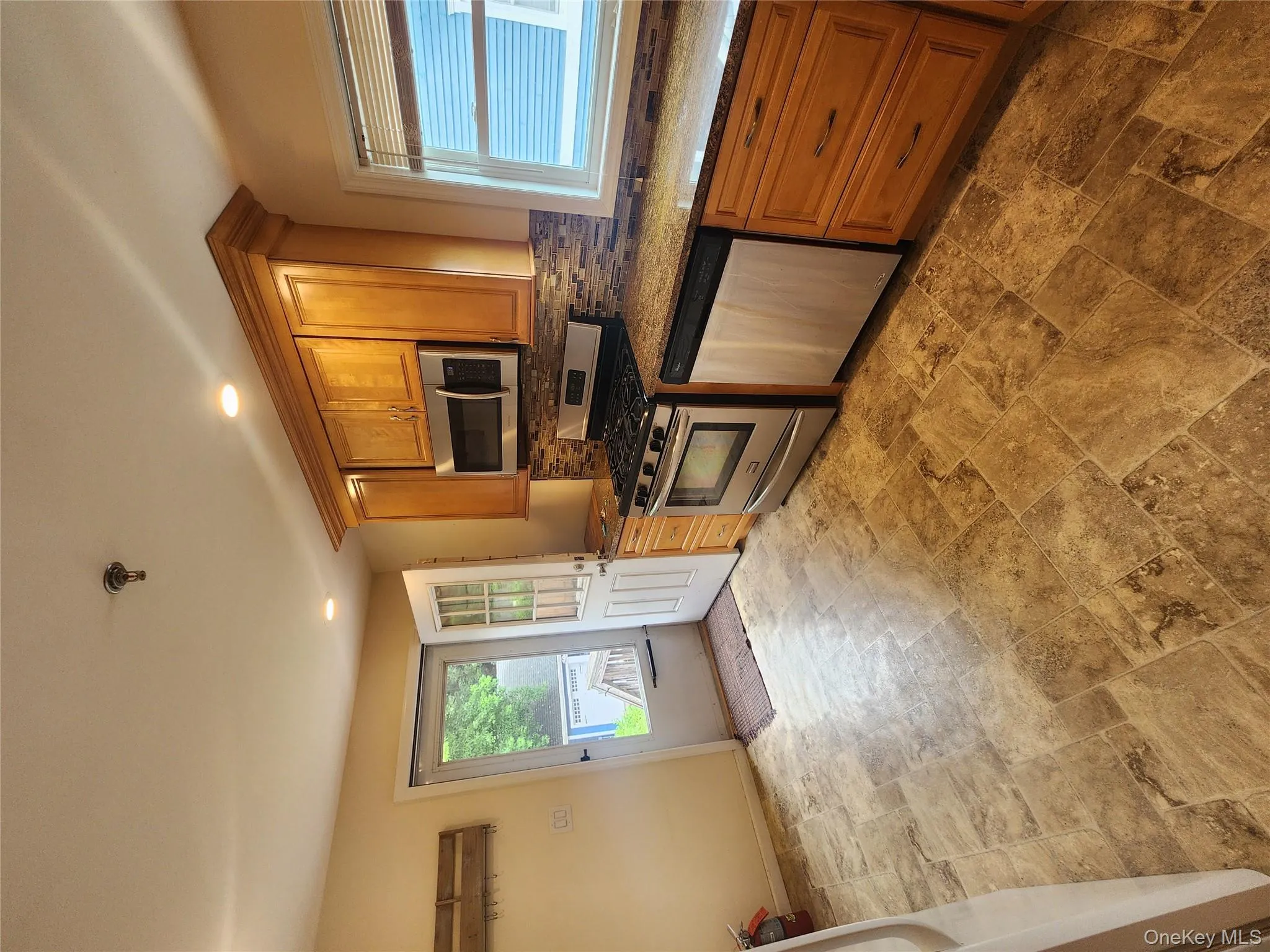 Kitchen with dishwasher, stainless steel range with gas cooktop, backsplash, light stone finish flooring, and brown cabinetry Kitchen with dishwasher, stainless steel range with gas cooktop, backsplash, light stone finish flooring, and brown cabinetry