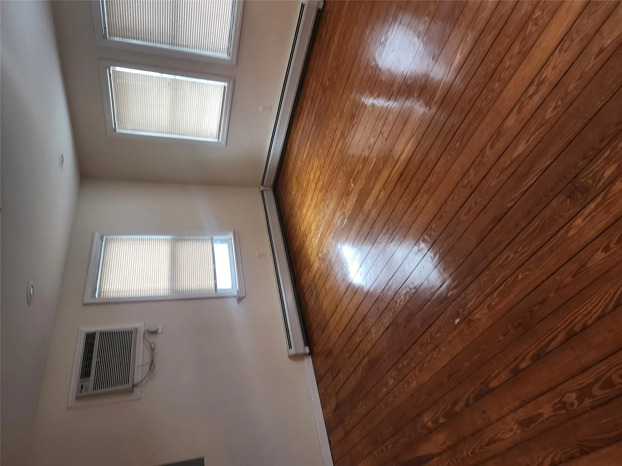 Empty room with baseboard heating, a wall mounted air conditioner, and hardwood / wood-style flooring Empty room with baseboard heating, a wall mounted air conditioner, and hardwood / wood-style flooring