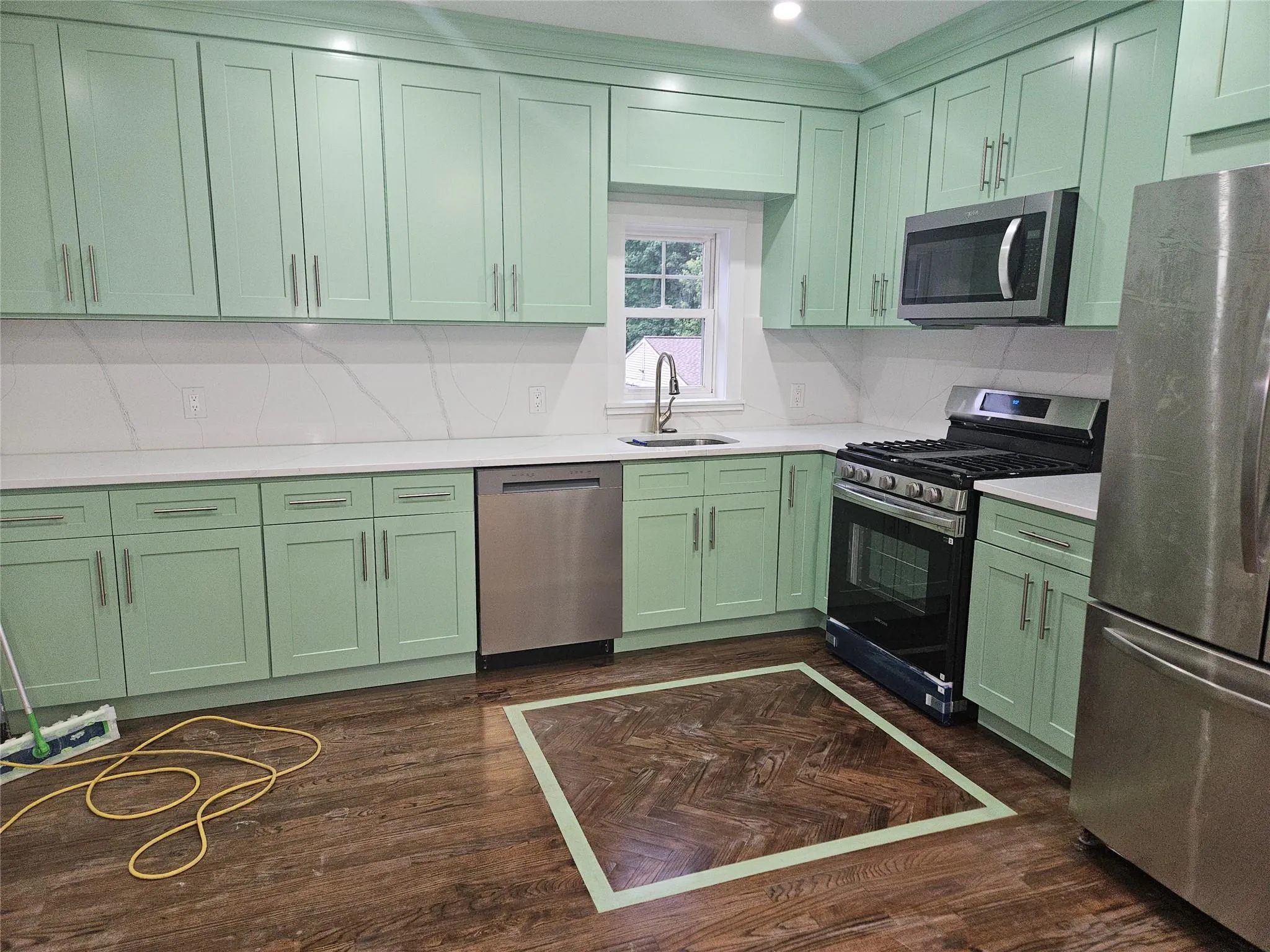 Kitchen with green cabinets, stainless steel appliances, a sink, light countertops, and tasteful backsplash Kitchen with green cabinets, stainless steel appliances, a sink, light countertops, and tasteful backsplash