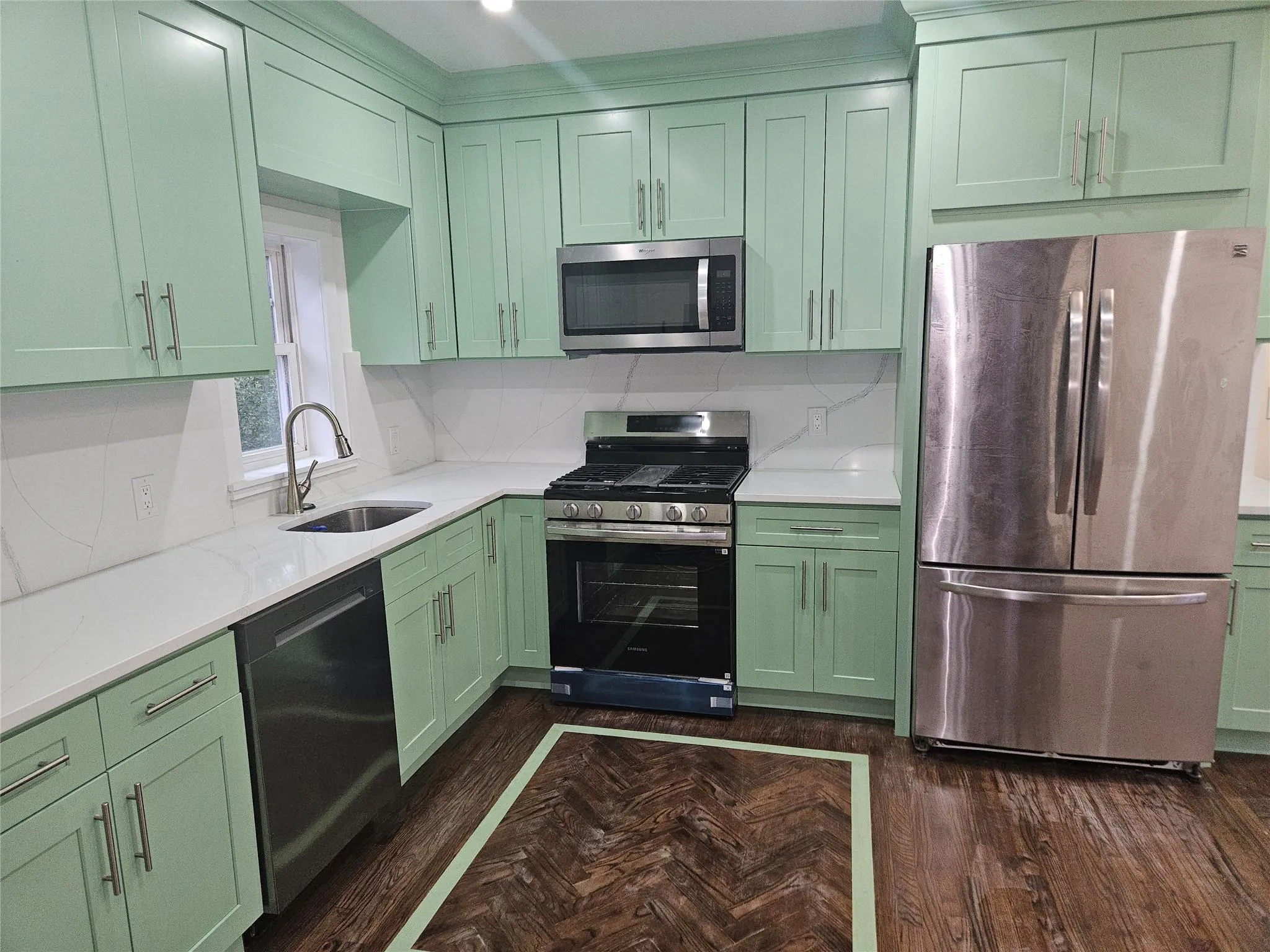 Kitchen featuring green cabinetry, appliances with stainless steel finishes, a sink, and light countertops Kitchen featuring green cabinetry, appliances with stainless steel finishes, a sink, and light countertops