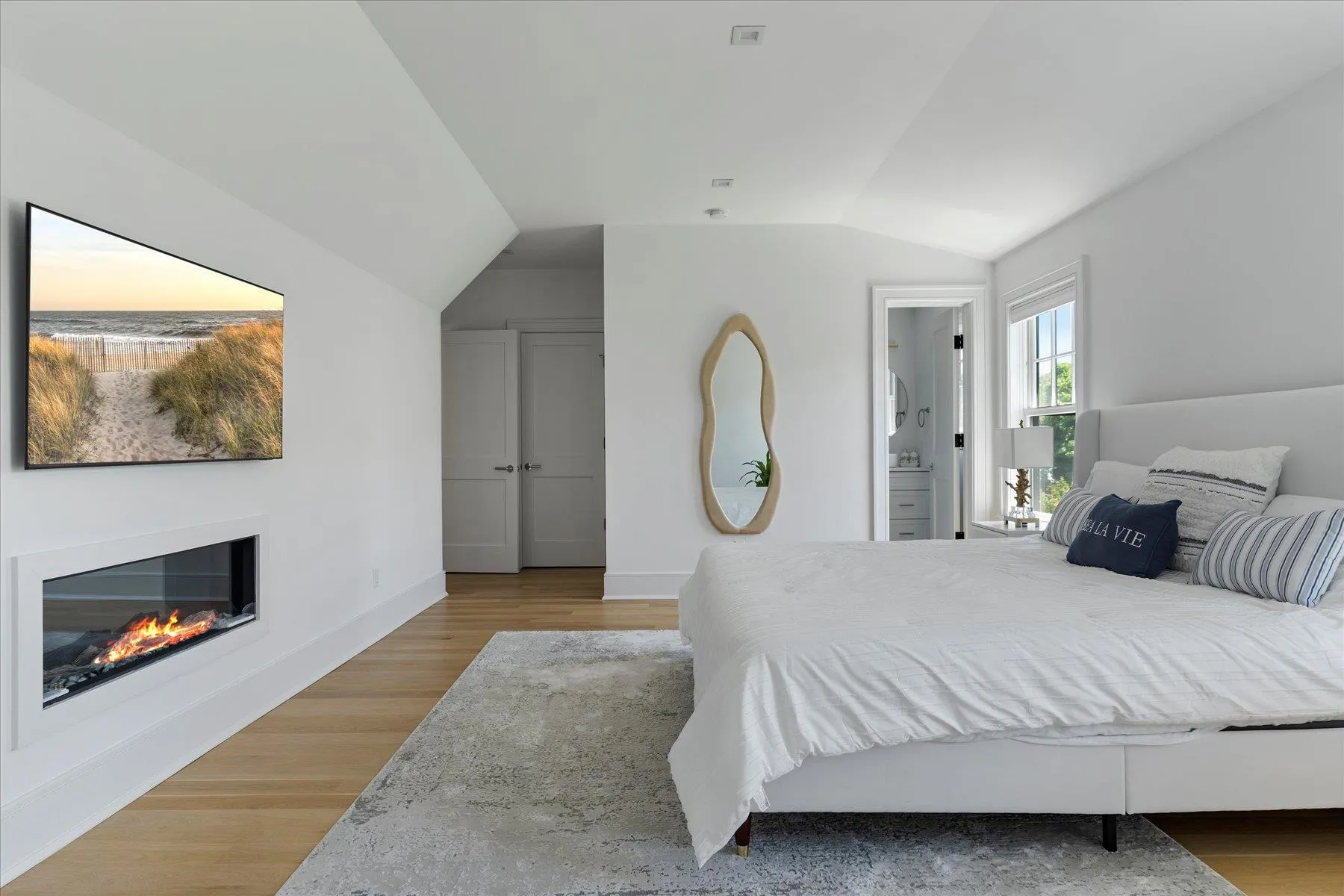 Bedroom with vaulted ceiling, light wood-type flooring, and a glass covered fireplace Bedroom with vaulted ceiling, light wood-type flooring, and a glass covered fireplace