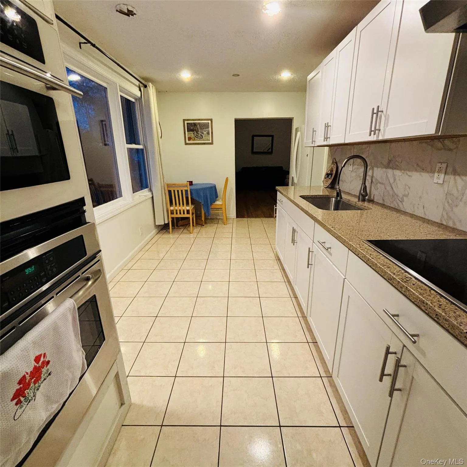 Kitchen with white cabinets, light tile patterned floors, light stone countertops, backsplash, and stainless steel (double oven- not included) Kitchen with white cabinets, light tile patterned floors, light stone countertops, backsplash, and stainless steel (double oven- not included)