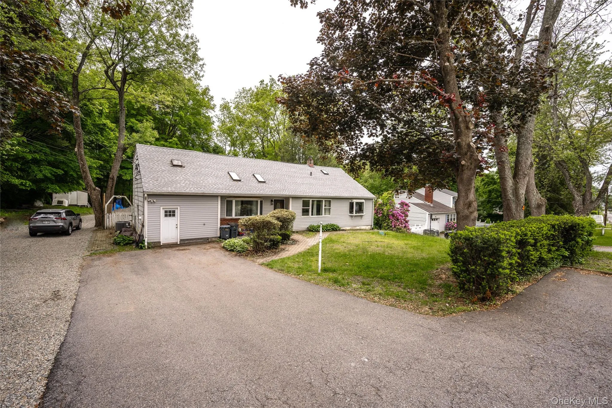 Ranch-style home with asphalt driveway, a shingled roof, a front lawn, and view of scattered trees Ranch-style home with asphalt driveway, a shingled roof, a front lawn, and view of scattered trees