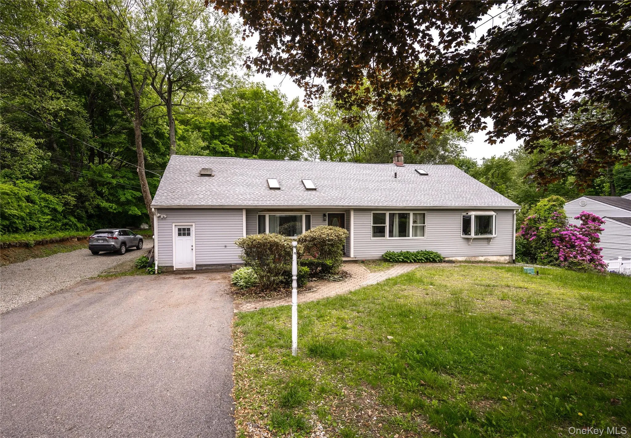 Single story home featuring a front lawn, a chimney, a shingled roof, and asphalt driveway Single story home featuring a front lawn, a chimney, a shingled roof, and asphalt driveway